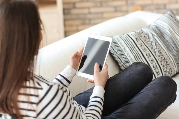 Mujer joven usando el comprimido mientras descansa en el sofá en casa — Foto de Stock