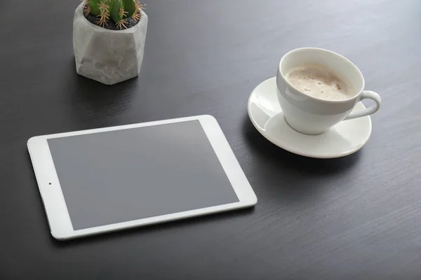 Tablet computer, cup of coffee and cactus on table