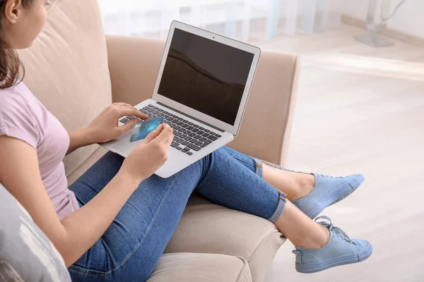 Young woman with credit card using laptop while resting on couch at home — Stock Photo, Image