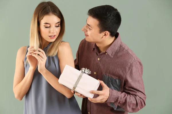 Young man giving present to his beloved girlfriend on color background — Stock Photo, Image