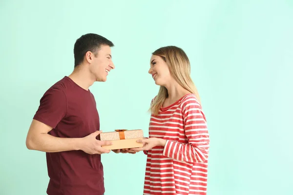 Young man giving present to his beloved girlfriend on color background — Stock Photo, Image