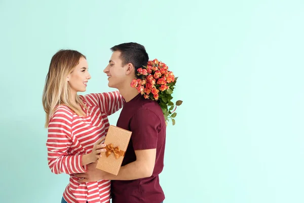愉快的年轻妇女与礼物盒和花拥抱她的男朋友在颜色背景 — 图库照片