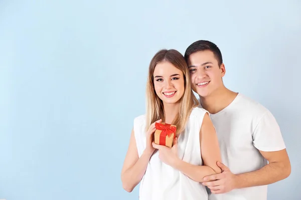 Happy young couple with gift box on color background — Stock Photo, Image