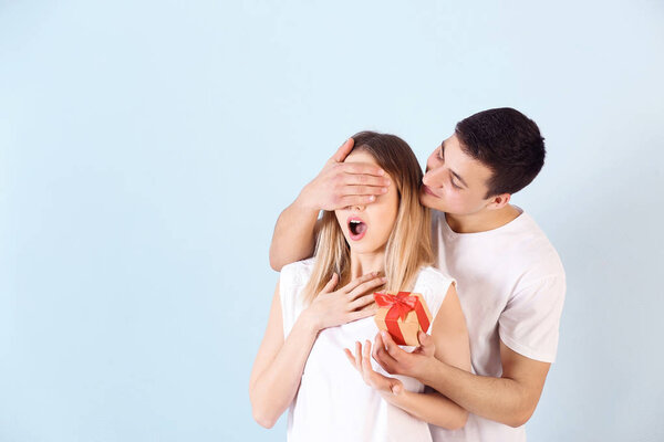 Молодой человек дарит подарок своей любимой девушке на цветном фоне
