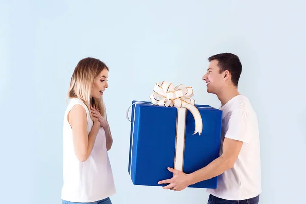 Young man giving present to his beloved girlfriend on color background — Stock Photo, Image