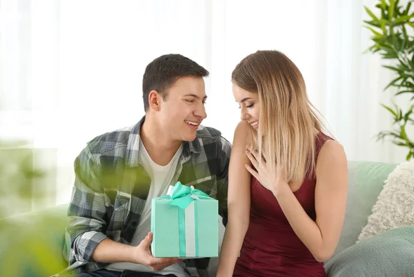 Joven hombre dando regalo a su amada novia en casa — Foto de Stock