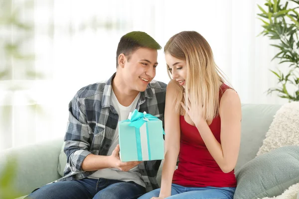 Joven hombre dando regalo a su amada novia en casa — Foto de Stock