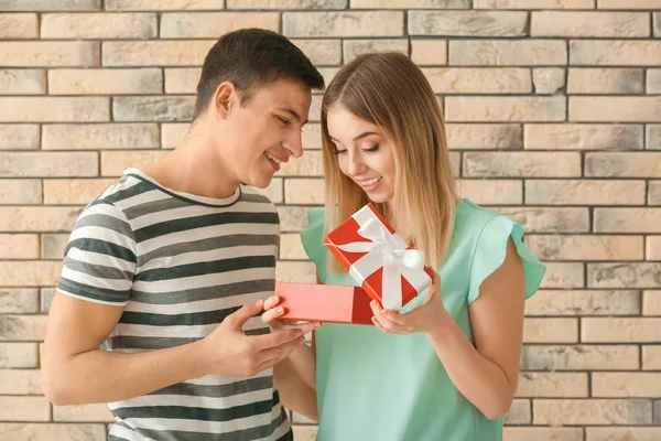 Young woman opening gift box from her boyfriend near brick wall — Stock Photo, Image