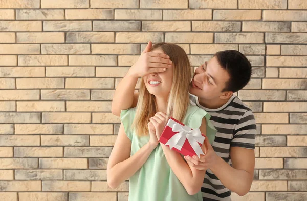 Young man giving present to his beloved girlfriend near brick wall — Stock Photo, Image