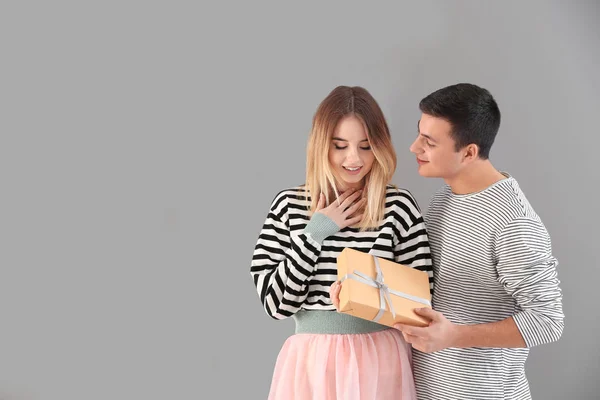 Молодой человек дарит подарок своей любимой девушке на сером фоне — стоковое фото