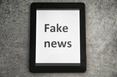 Tablet with text Fake NEWS on screen against grey background clipart