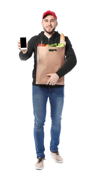 Junger Mann mit Produkten in Papiertüte und Handy auf weißem Hintergrund. Essenslieferdienst — Stockfoto