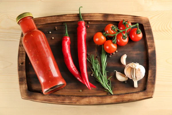 Fles met lekkere saus en groenten op houten bord — Stockfoto