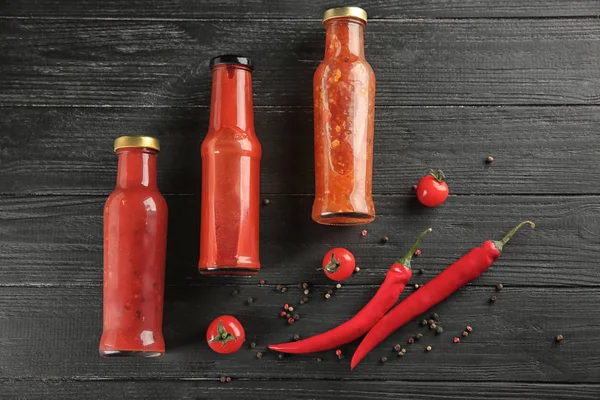 Bottles with different sauces and vegetables on wooden background, flat lay