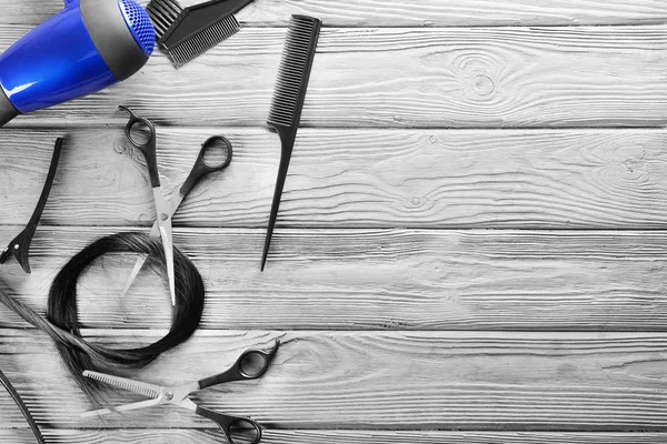 Пласка композиція з інструментами перукаря та ниткою чорного волосся на дерев'яному фоні — стокове фото