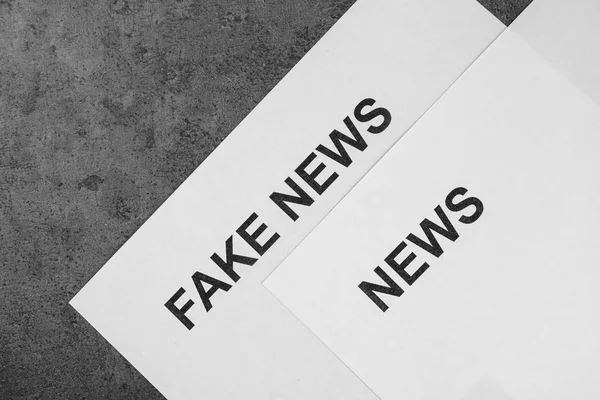 Sheets of paper with words FAKE and NEWS on gray background — Stock Photo, Image