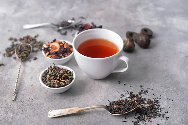 Composition with different types of dry tea and delicious beverage on grey background — Stock Photo, Image