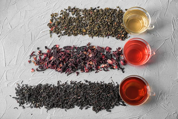 Plochá laických složení s různými typy suchého čaje a poháry na šedém pozadí — Stock fotografie