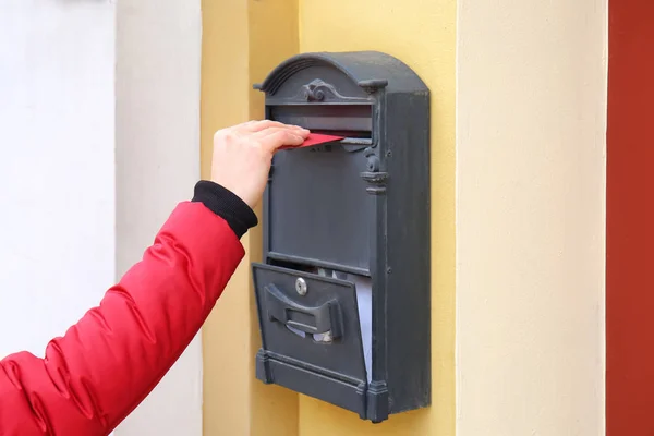 Woman putting envelope into mailbox on wall of building outdoors — Stock Photo, Image