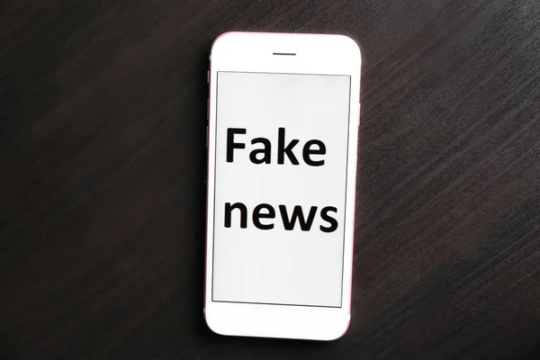 Phone with text FAKE NEWS on screen against dark background — Stock Photo, Image