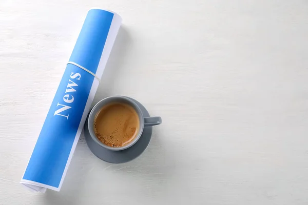 Roll of papers with word NEWS and cup of coffee on wooden table