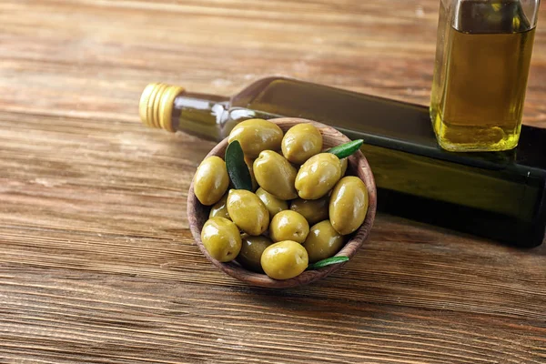 Bottles with oil and olives on wooden table — Stock Photo, Image