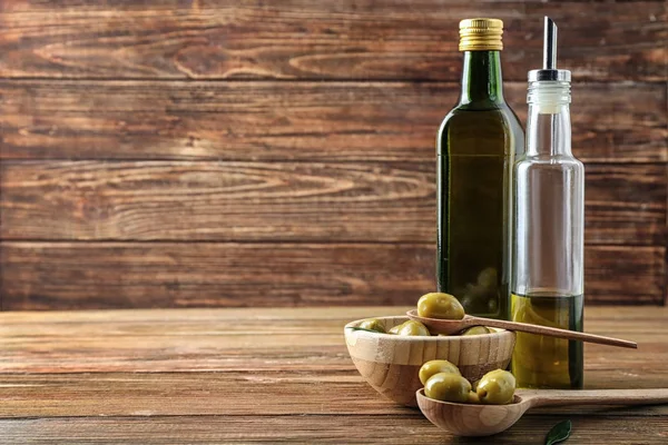 Botellas con aceite y aceitunas sobre mesa de madera — Foto de Stock