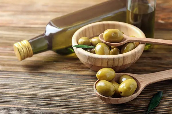 Bowl and spoons with fresh olives on wooden table — Stock Photo, Image