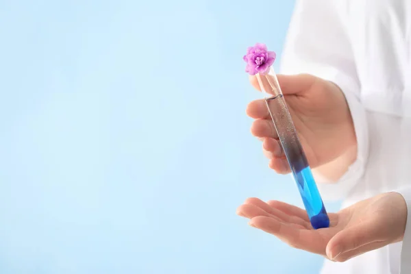 Scientist holding test tube with flowers on color background — Stock Photo, Image