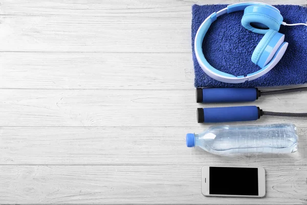 Composición plana con botella de agua, cuerda de salto, auriculares y smartphone sobre fondo de madera. Entrenamiento en el gimnasio — Foto de Stock