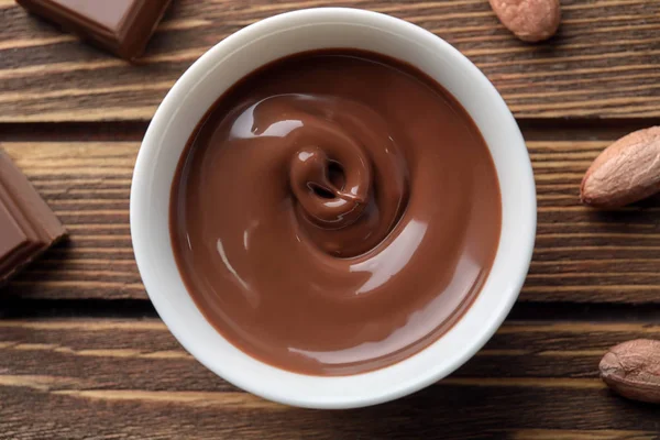 Bowl with tasty melted chocolate on wooden table, top view — Stock Photo, Image