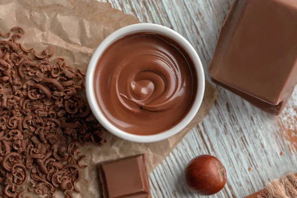 Kom met smakelijk gesmolten chocolade op houten achtergrond — Stockfoto