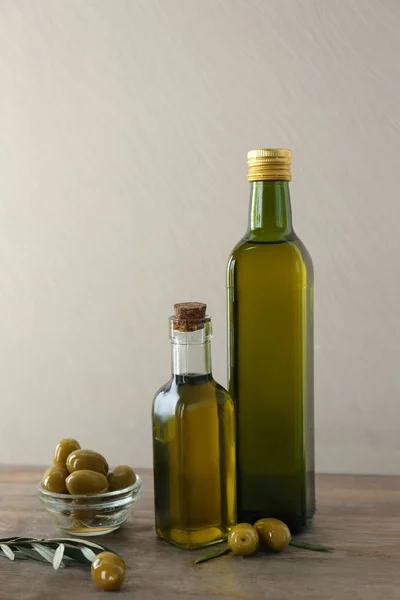 Botellas con aceite y aceitunas frescas sobre mesa de madera sobre fondo claro — Foto de Stock