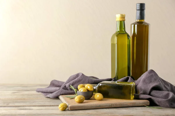 Botellas con aceite y aceitunas frescas sobre mesa de madera sobre fondo claro — Foto de Stock