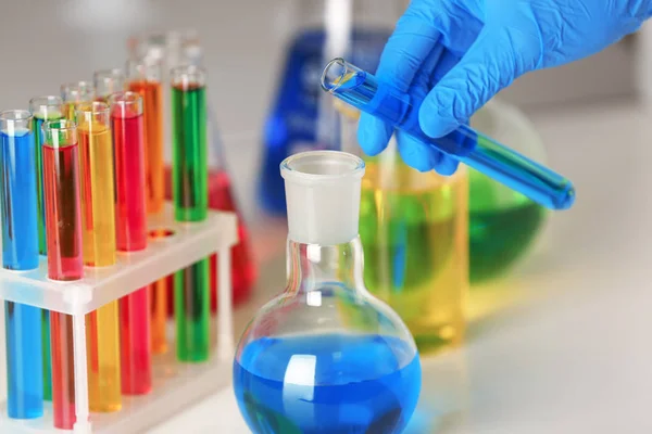 Laboratorium werknemer vloeistof uit de reageerbuis binnenstromen kolf aan tafel, close-up — Stockfoto