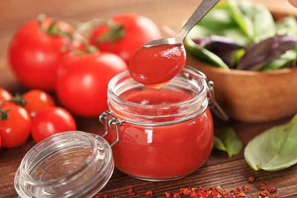 Glass jar and spoon with red sauce, closeup — Stock Photo, Image