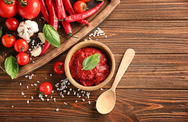 Deliciosa salsa roja en tazón e ingredientes sobre fondo de madera, vista superior — Foto de Stock