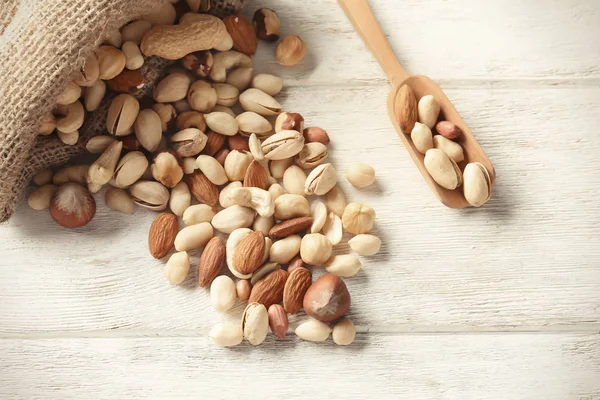 Sack and scoop with different nuts on wooden table — Stock Photo, Image