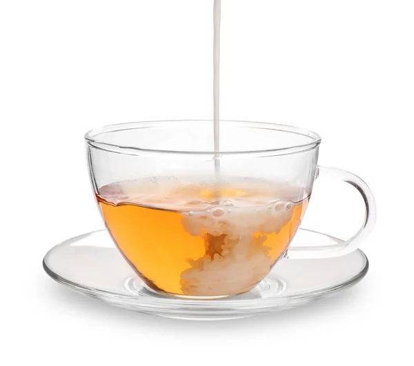 Verter leche en una taza de vidrio con té aromático sobre fondo blanco — Foto de Stock