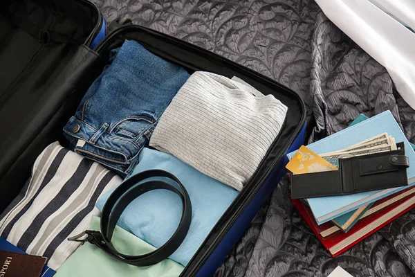 Brieftasche, Bücherstapel und offener Koffer mit gepackten Sachen auf dem Bett — Stockfoto