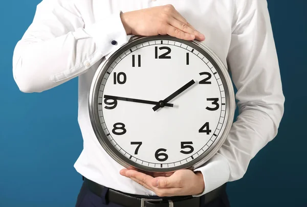Hombre sosteniendo el reloj en el fondo de color. Concepto de gestión del tiempo — Foto de Stock