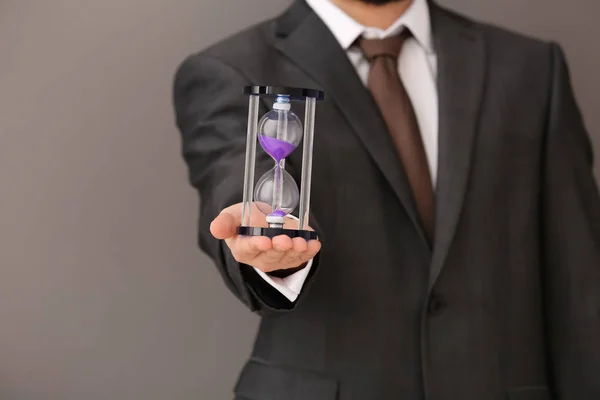 Man holding hourglass on gray background. Time management concept — Stock Photo, Image