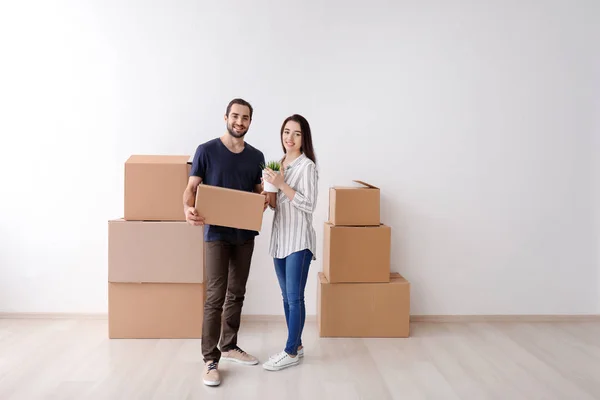 Young couple with boxes and houseplant indoors. Moving into new house — Stock Photo, Image