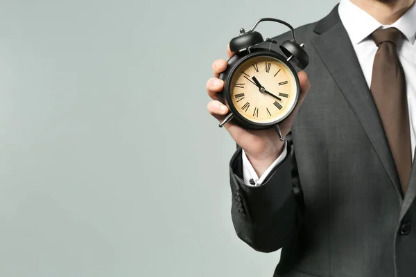 Hombre sosteniendo reloj sobre fondo gris. Concepto de gestión del tiempo — Foto de Stock