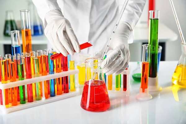 Assistante de laboratoire versant le liquide de l'éprouvette dans la fiole à table — Photo