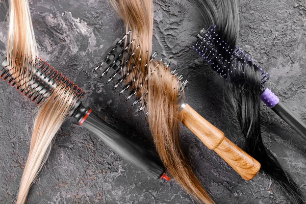 Different brushes and strands of hair on grey textured background — Stock Photo, Image