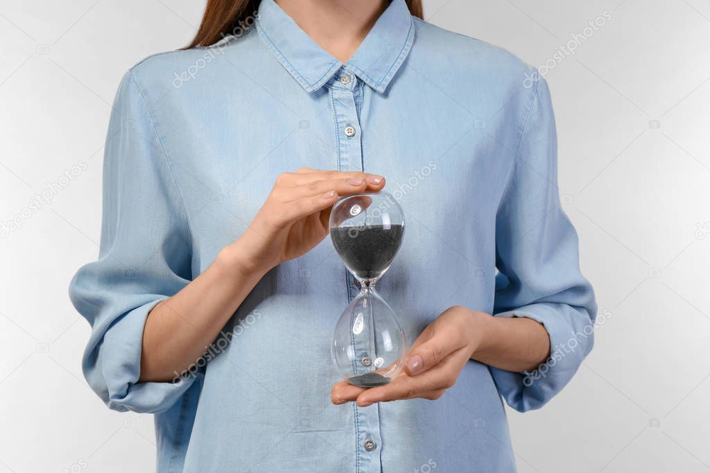 Woman holding hourglass on light background. Time management concept