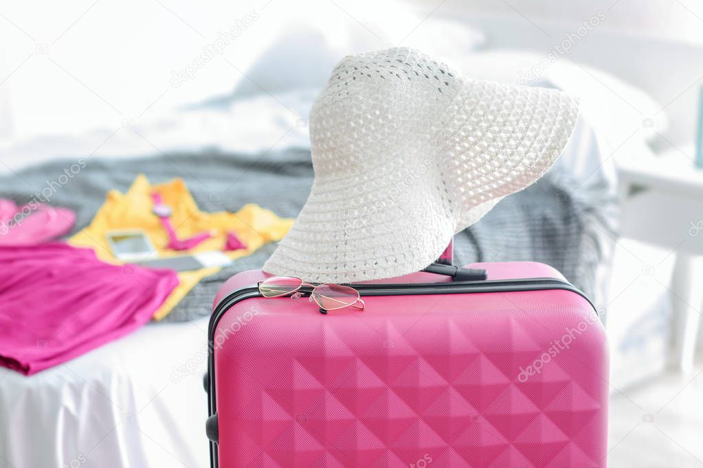 Beach hat and sunglasses on travel suitcase indoors