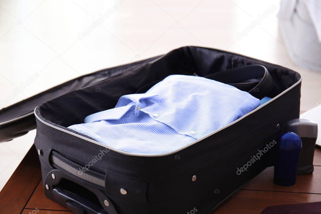 Open travel suitcase with clothes on wooden table