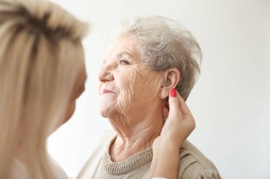 Otolaryngologist işitme cihazı üst düzey kadının kulağına ışık arka plan üzerine koyarak.
